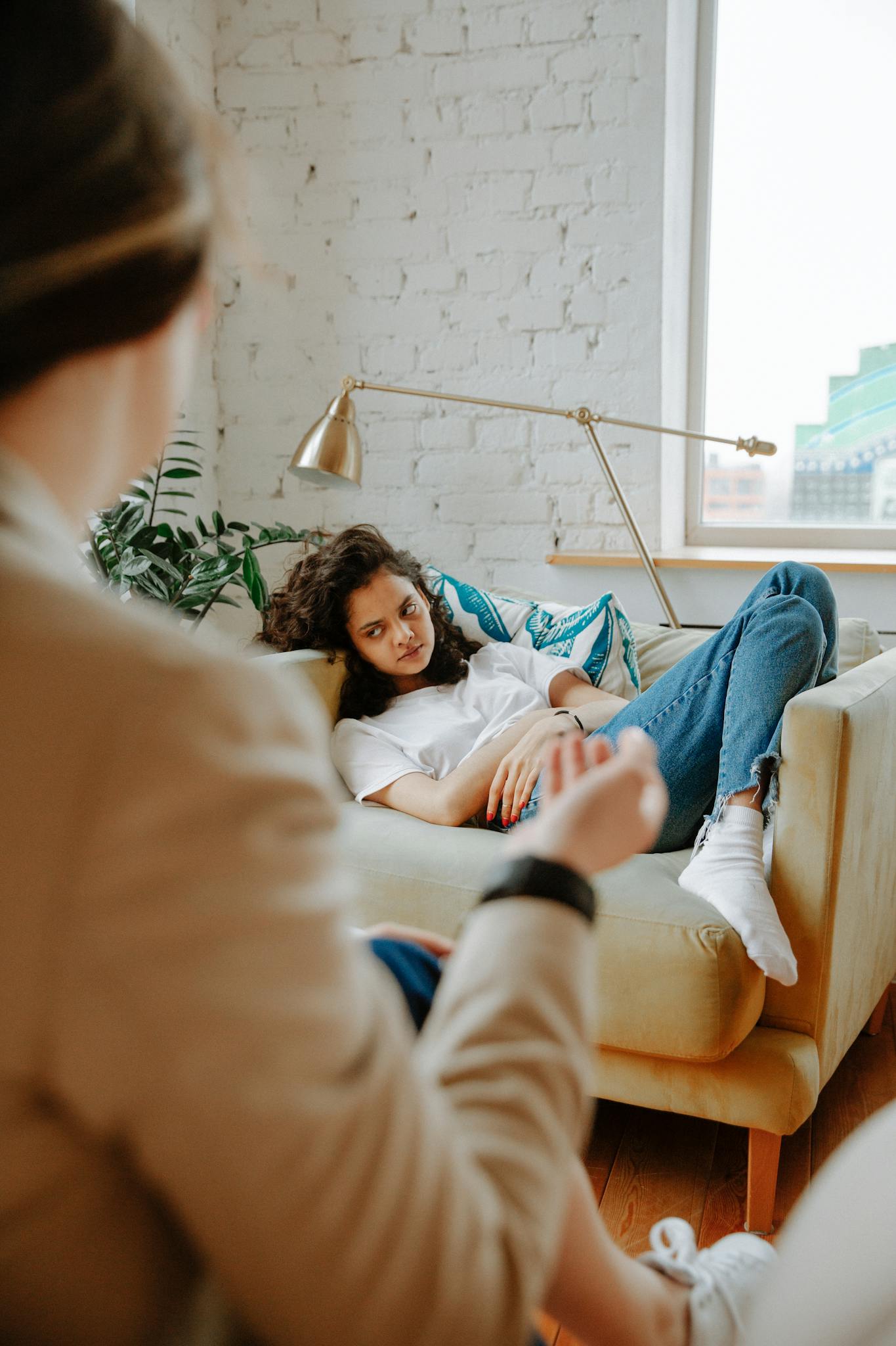 A therapist converses with a young adult on a sofa, focusing on mental health.